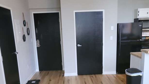 A kitchen with wooden flooring, a black refrigerator, and a trash bin. - Honeycomb Hideout (Cleveland)