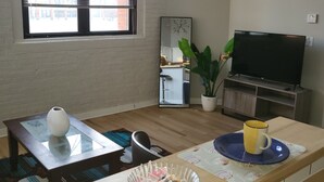 A living room with a TV, a coffee table, a bowl of candies, a yellow mug, and a large window with blinds. - Honeycomb Hideout (Cleveland)