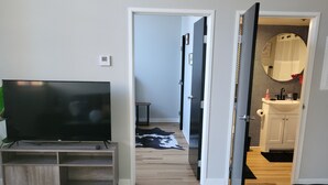 A modern living room with a flat-screen TV on a wooden stand, a patterned rug, and a hallway leading to a bathroom with a sink and mirror. - Honeycomb Hideout (Cleveland)