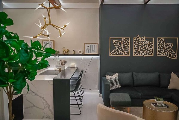 Un salon moderne avec un canapé foncé, une table basse ronde et un coin repas doté d’un comptoir en marbre et de chaises.