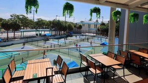 An outdoor tennis court with multiple courts, seating areas, and hanging plants.
