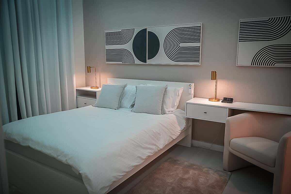 A modern bedroom with a bed, bedside tables, a chair, and abstract wall art.