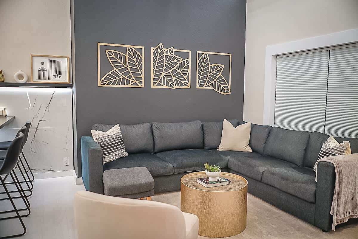 Un salon moderne avec un canapé d’angle gris foncé, une table basse ronde et une décoration murale minimaliste.
