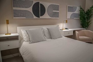 Une chambre à coucher comprenant un lit, des tables de chevet, un bureau, une chaise et des œuvres d’art abstraites accrochées au mur.