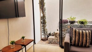 Ein Wohnzimmer mit Flachbildfernseher, einer Couch mit gestreiftem Kissen und einem kleinen Tisch mit zwei Blumentöpfen.