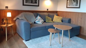 A cozy living room with a blue sofa, two small wooden tables, and a white rug. There are two framed pictures on the walls and a lamp on a side table. - La Valériane 103 - Beautiful 2-room apartment with an open view of the valley (LES AVANCHERS VALMOREL)