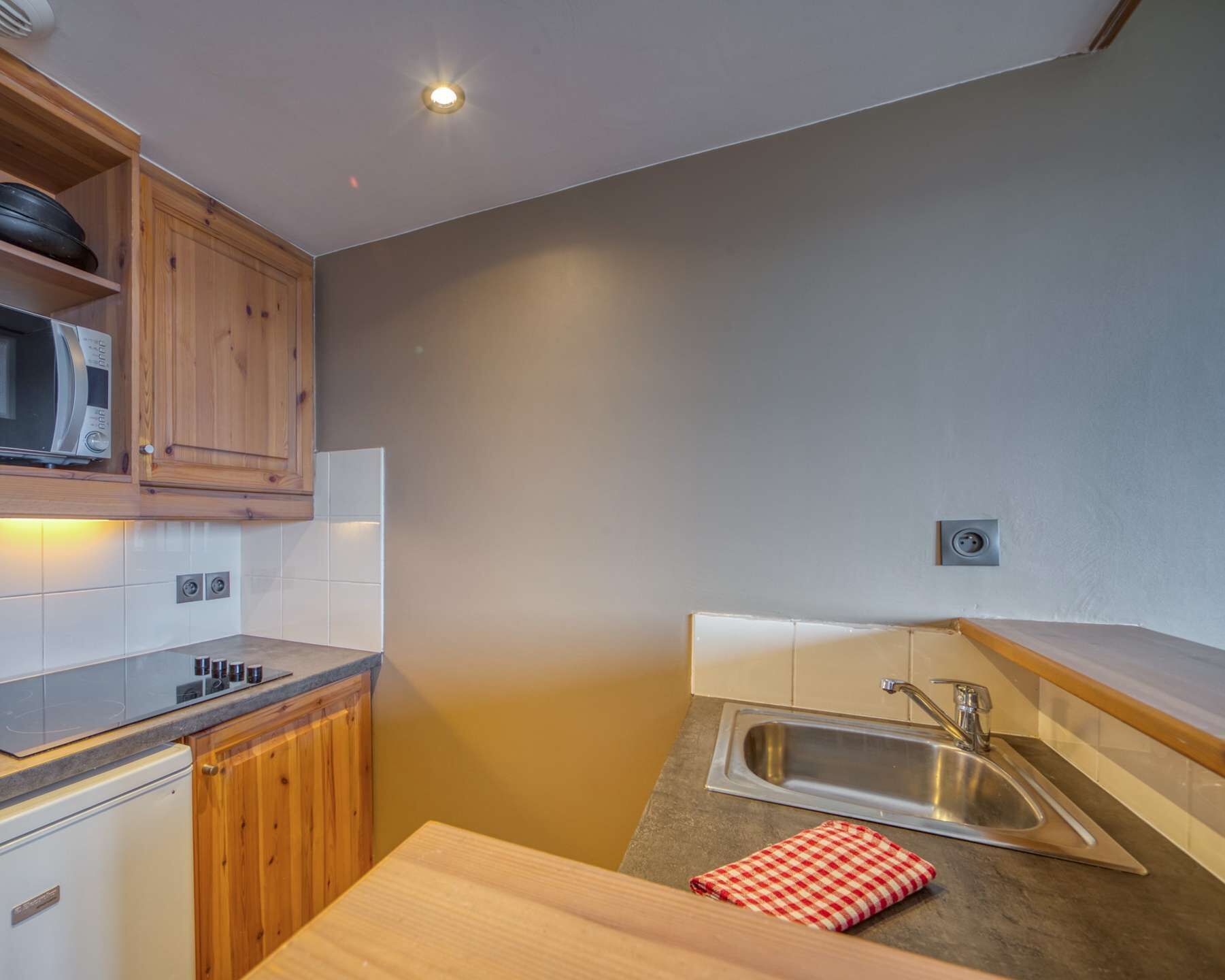 A compact kitchen with wooden cabinets, a built-in microwave, a stainless steel sink, and a small countertop.