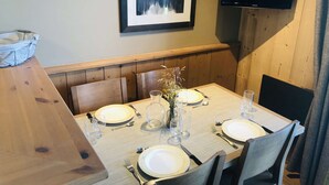 A dining area with a wooden table set for four, a framed picture on the wall, and a flat-screen TV mounted above the table. - La Valériane 103 - Beautiful 2-room apartment with an open view of the valley (LES AVANCHERS VALMOREL)