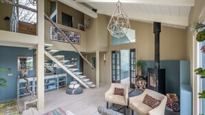 Een ruime woonkamer met een trap, een open haard en diverse zitmogelijkheden.