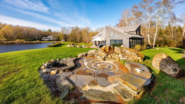 Een modern huis met een vuurkorf van natuursteen en uitzicht op een meer.