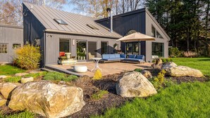 Een modern huis met een terras, zitplaatsen buiten en een grote parasol.