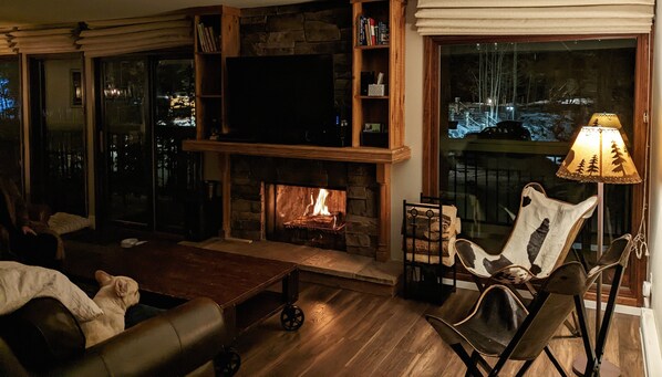 Un salon chaleureux avec une cheminée en pierre, un téléviseur et des fauteuils confortables.