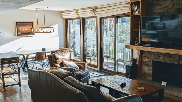 A modern living room with a large sectional sofa, a wooden coffee table, and a flat-screen TV mounted on a stone wall. - Beautiful, Quiet Condo in Keystone! (Keystone)