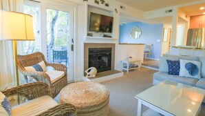 A living room with wicker furniture, a fireplace, a flat-screen TV, and a sofa with decorative pillows.