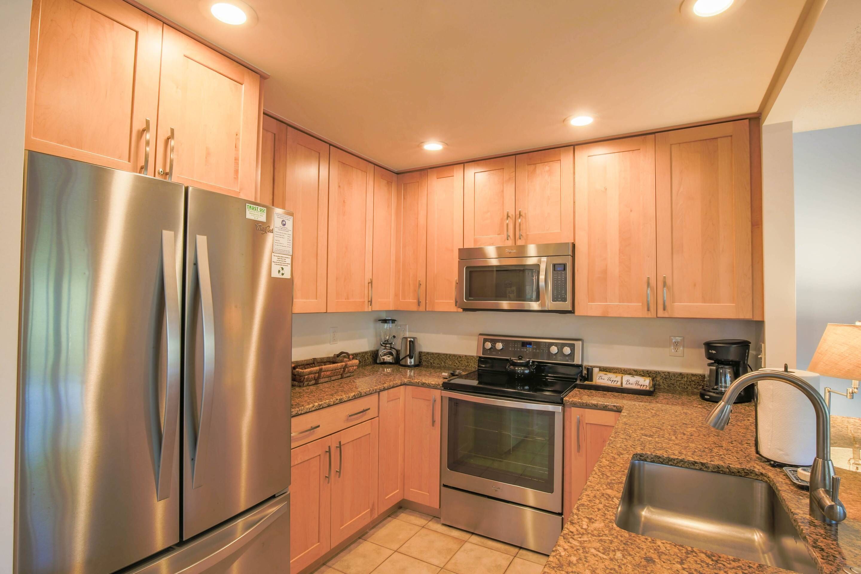 A kitchen with stainless steel appliances, wooden cabinets, granite countertops, and a sink.