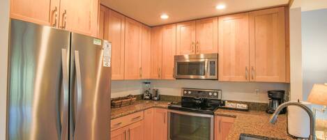 A kitchen with stainless steel appliances, wooden cabinets, granite countertops, and a sink.