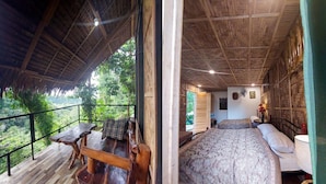 A wooden cabin with a balcony overlooking a forest, a bed with a patterned bedspread, and a small table with chairs. - Venida Farms by SMS Hospitality (Iligan)