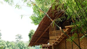 A rustic bamboo structure with a thatched roof, wooden staircase, and a small table with a red cloth. - Venida Farms by SMS Hospitality (Iligan)