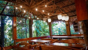 An indoor dining area with wooden tables and benches, a thatched roof, and hanging lights. - Venida Farms by SMS Hospitality (Iligan)
