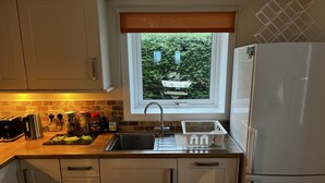 A kitchen with a window, a sink, a refrigerator, and a countertop with various items. - Hugh’s Highland Hideaway (Culnacnoc)