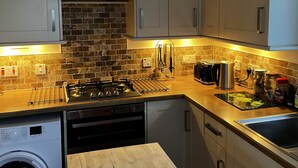 A modern kitchen with a built-in washing machine, a wooden countertop, and a brick backsplash. - Hugh’s Highland Hideaway (Culnacnoc)