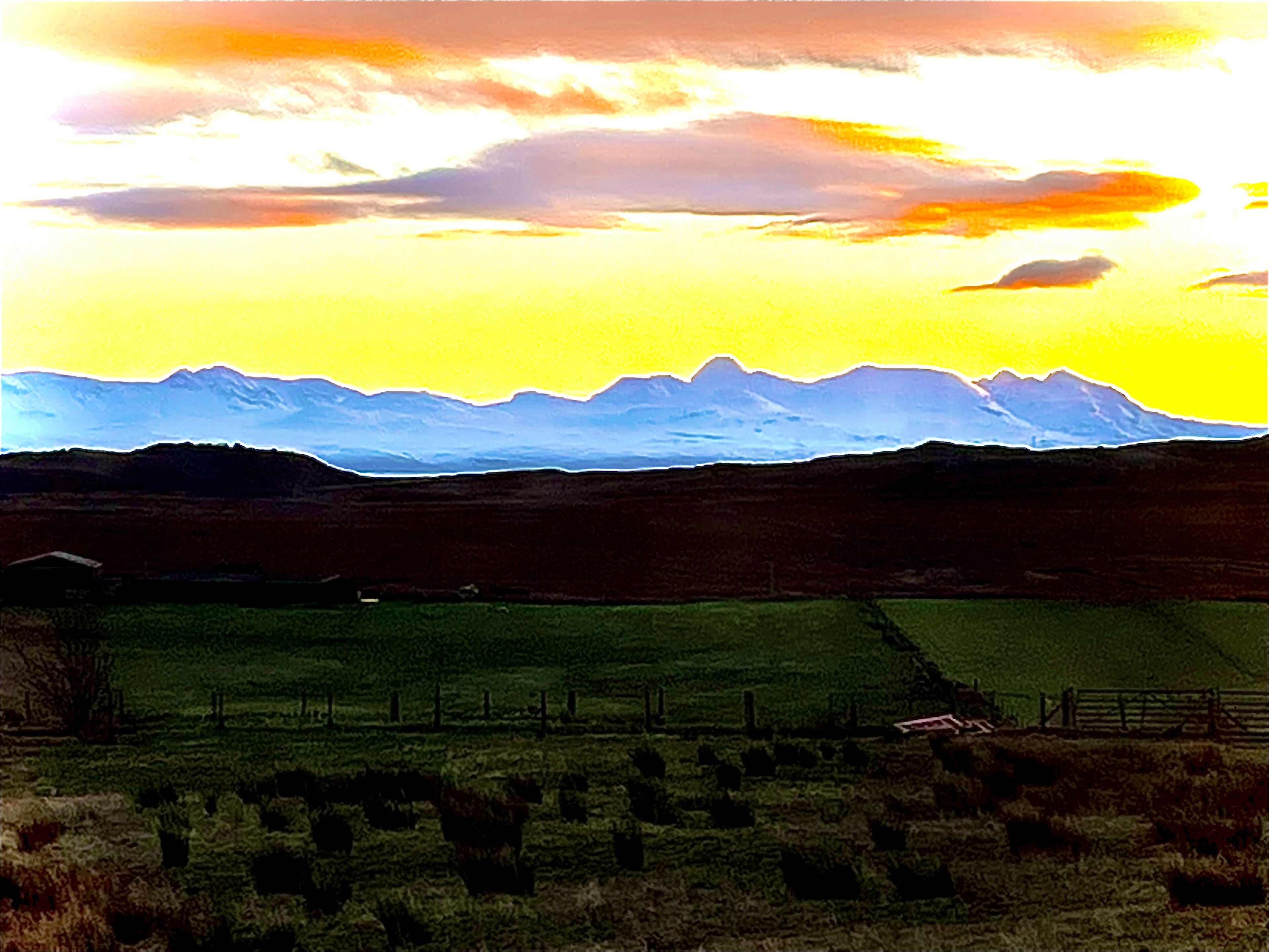 Paesaggio rurale con un campo, una recinzione e montagne in lontananza.