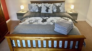 A neatly made bed with a headboard, two bedside tables with lamps, and a red wall. - Hugh’s Highland Hideaway (Culnacnoc)