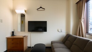 A hotel room with a flat-screen TV mounted on the wall, a wooden dresser, a bench, and a sofa. - Tabist Business Hotel Osamura (Sabae)
