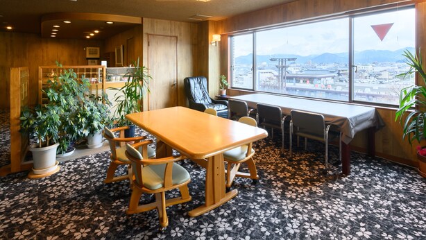 A conference room with a large table, chairs, potted plants, and a view of a cityscape through a large window. - Tabist Business Hotel Osamura (Sabae)