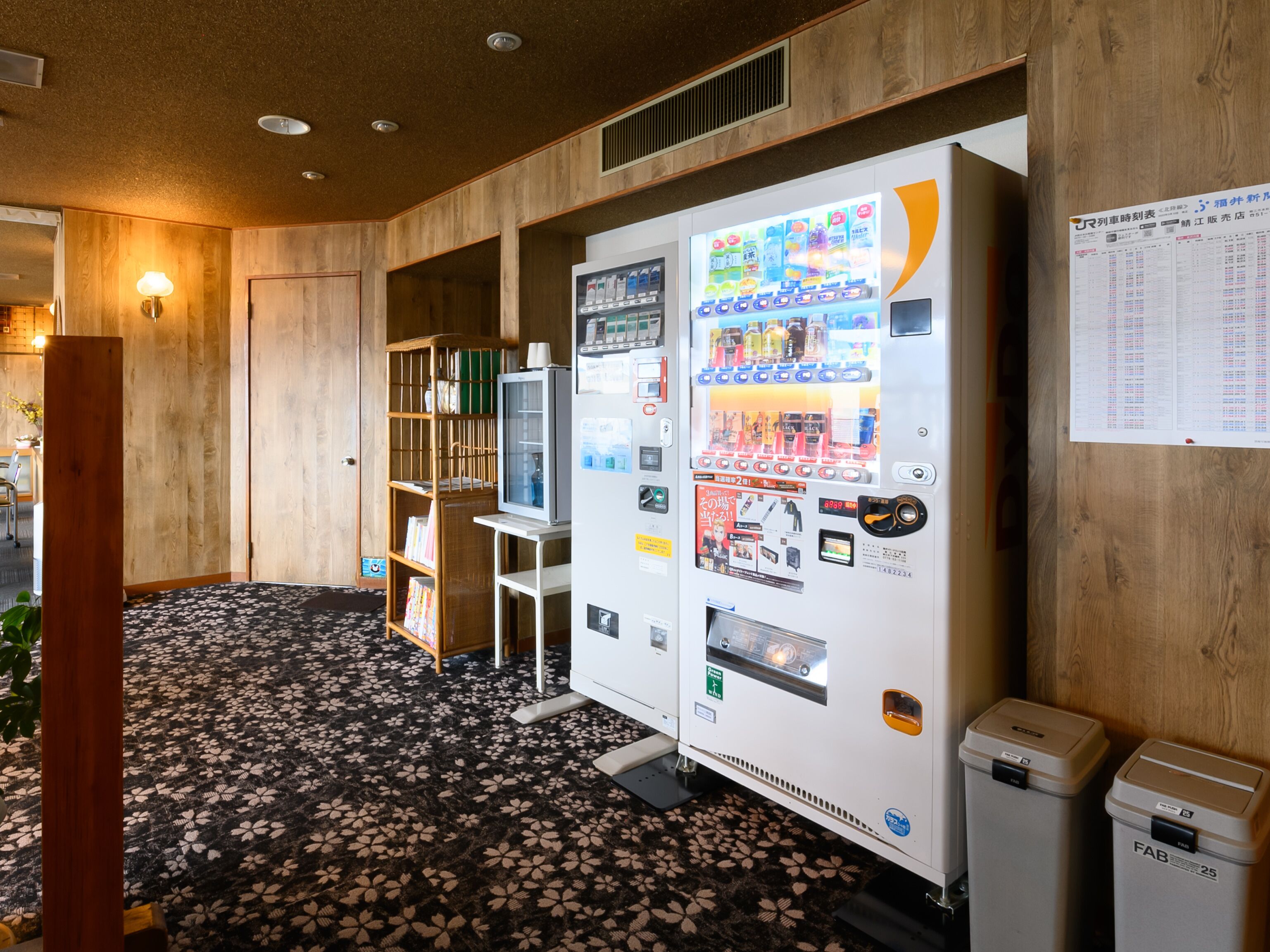 A vending machine with a selection of beverages and snacks, a small television, and a trash bin.