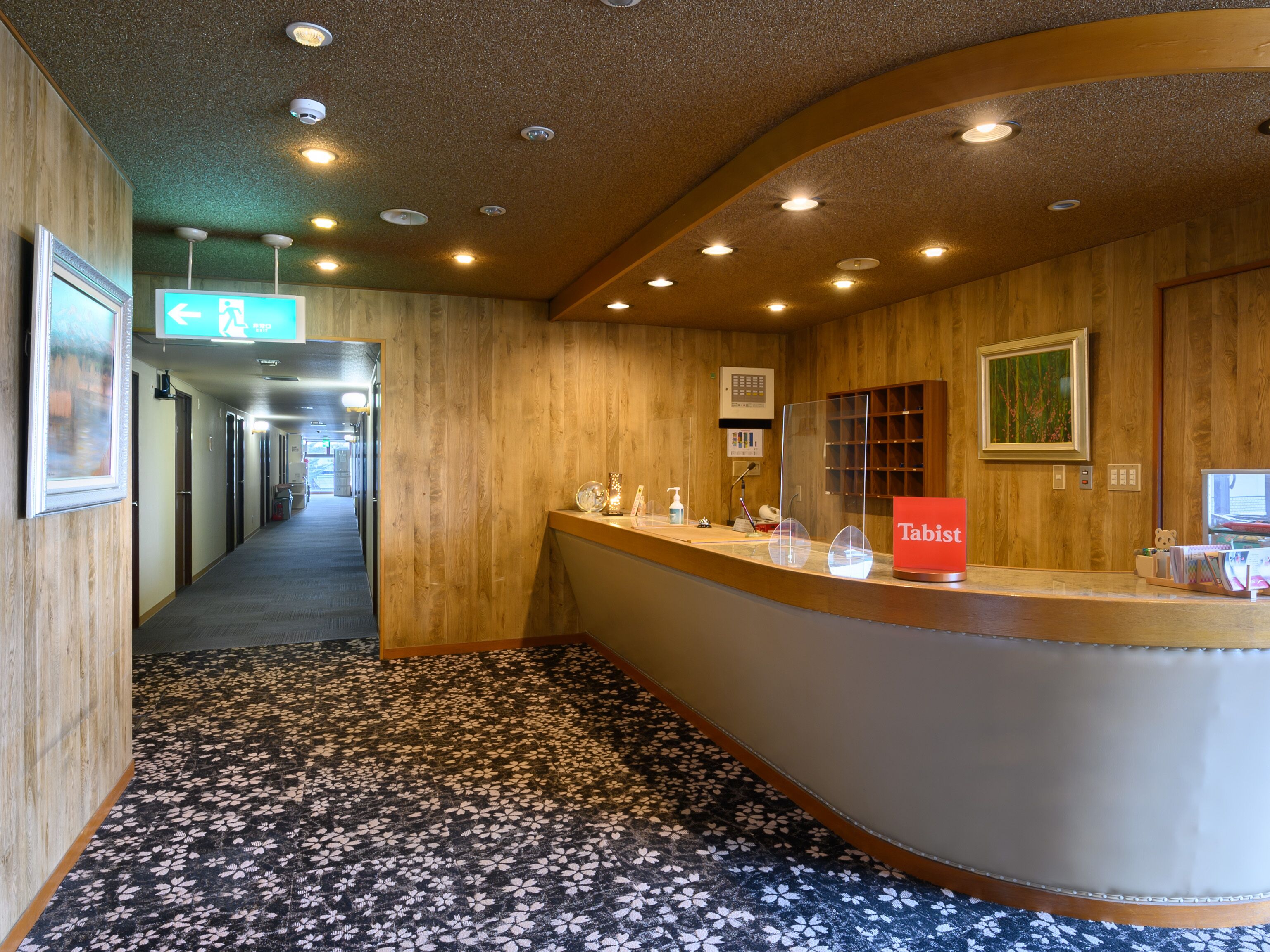 A hotel reception area with a wooden interior, a reception desk, a sign reading "Tabist", and a carpeted floor.