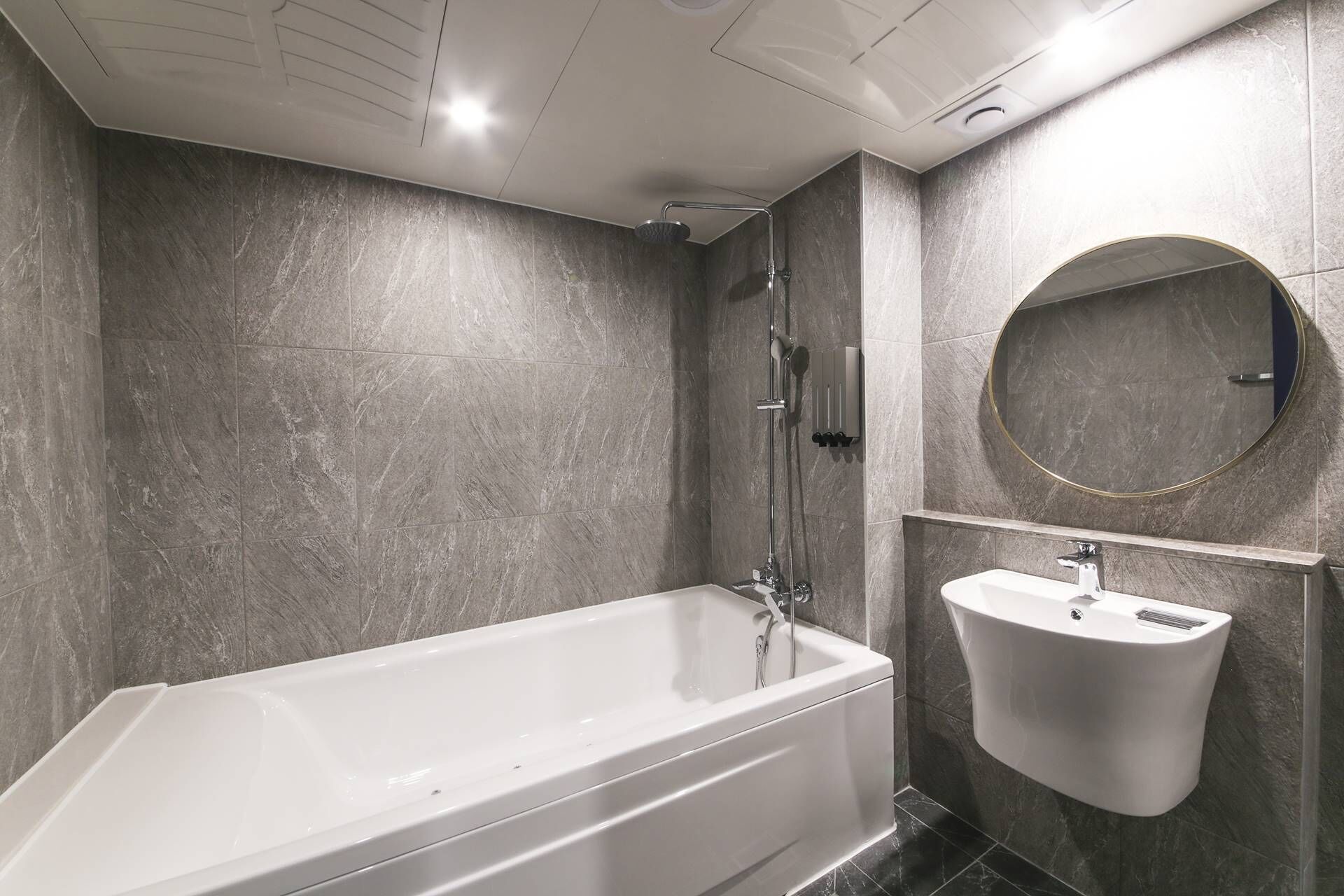 A modern bathroom with a bathtub, a wall-mounted sink, and a round mirror.
