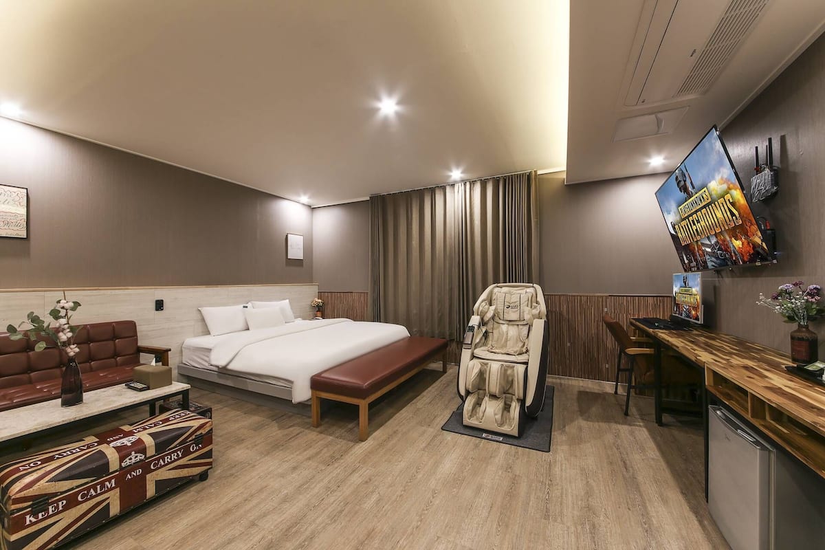 A hotel room with a bed, a massage chair, a TV, a desk, and a couch.