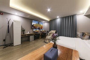 Habitación de hotel con cama, escritorio, silla, televisor y ventana con cortinas.