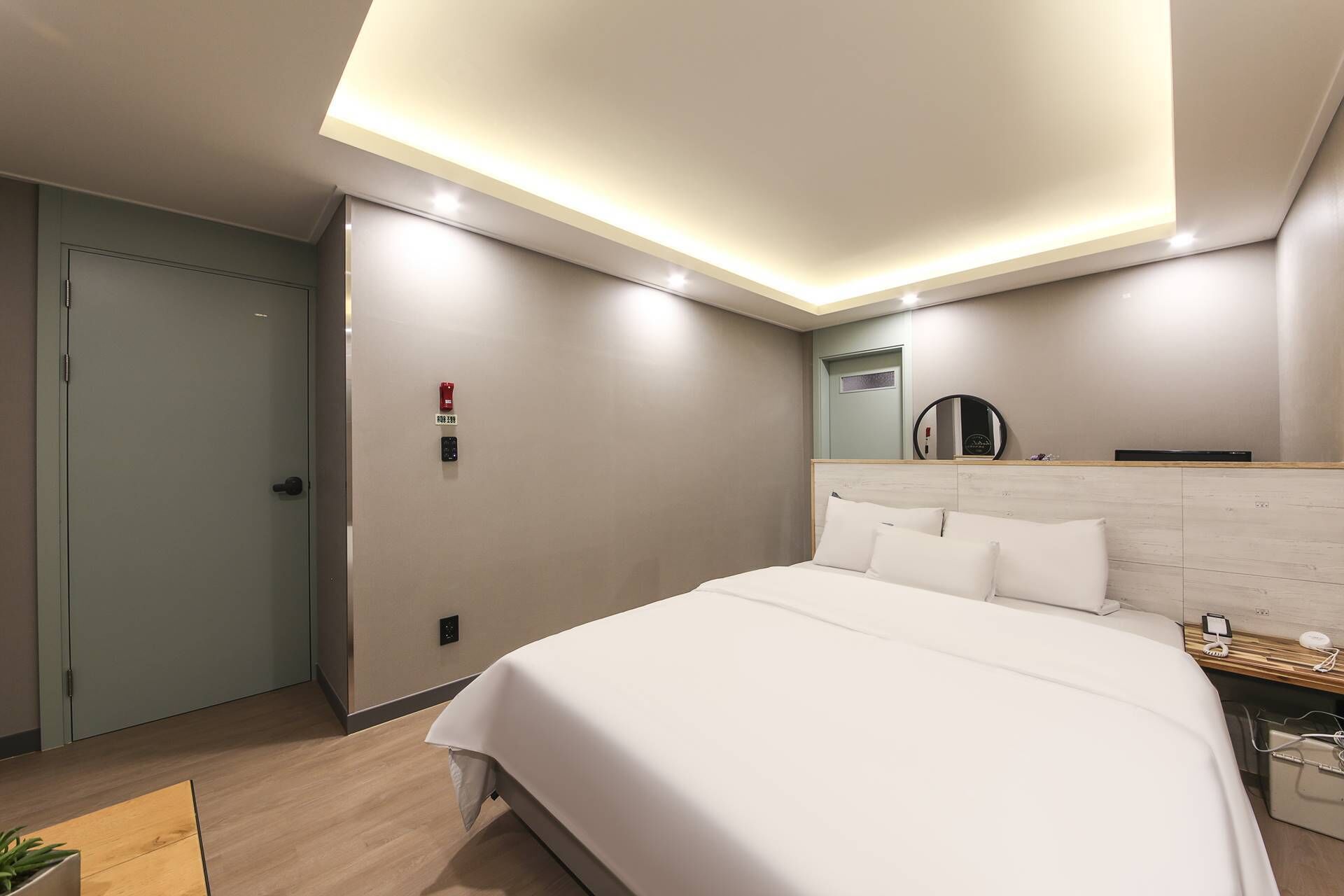 Una habitación de hotel moderna con una cama grande, una mesita de noche, un espejo y una lámpara en el techo.