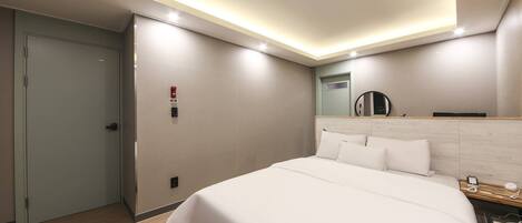 Una habitación de hotel moderna con una cama grande, una mesita de noche, un espejo y una lámpara en el techo.