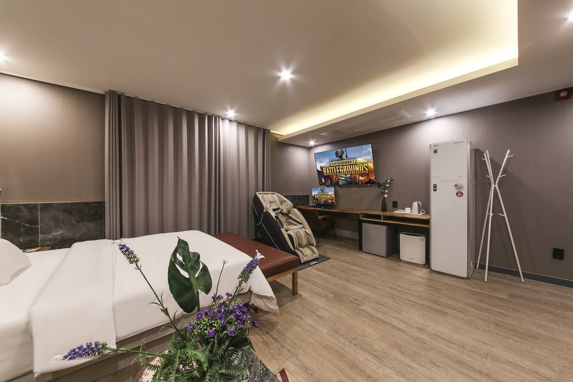 Une chambre d’hôtel moderne équipée d’un lit, d’un bureau, d’une chaise, d’un réfrigérateur et d’une grande affiche représentant un jeu vidéo.