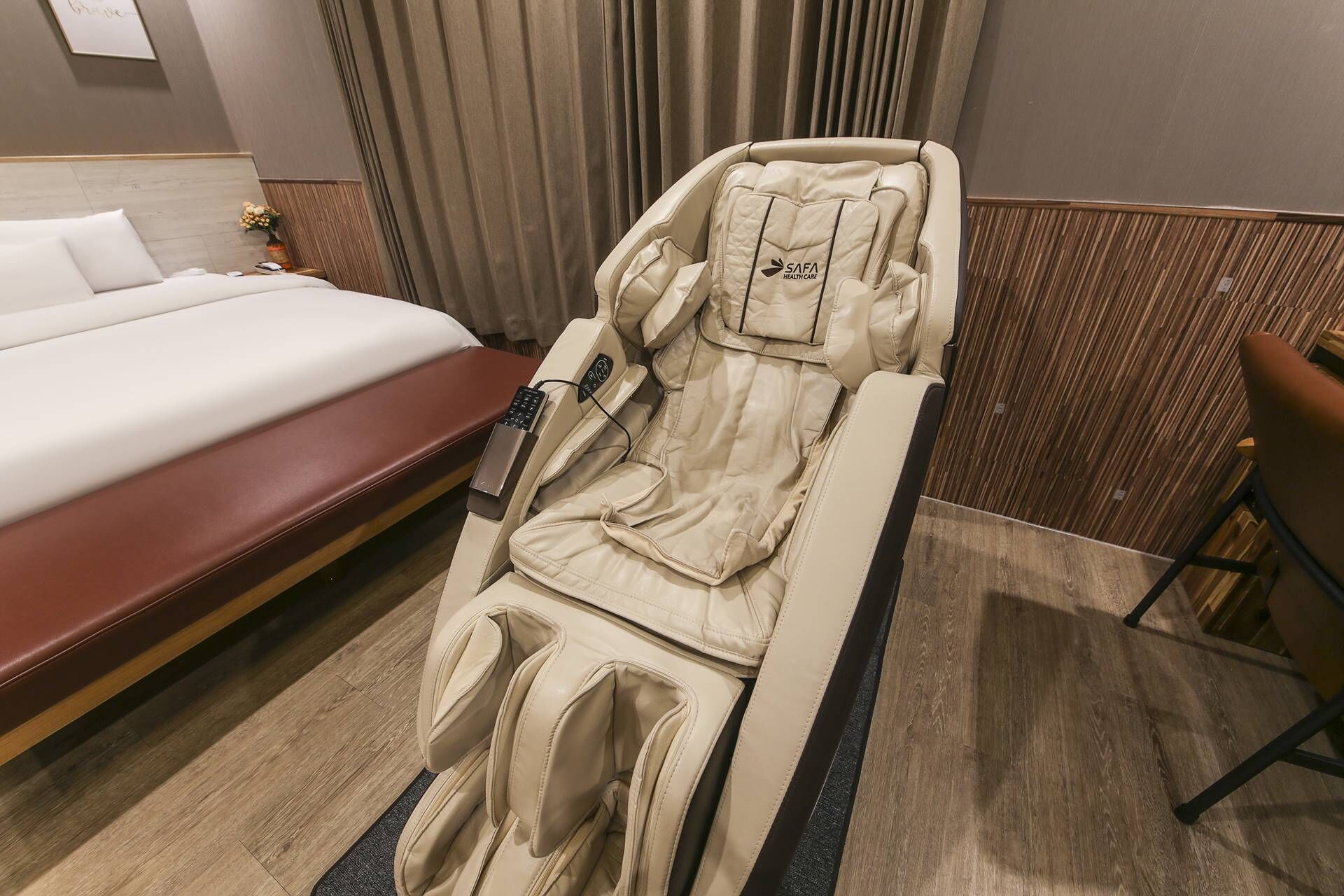 A hotel room with a massage chair, a bed, and a desk.