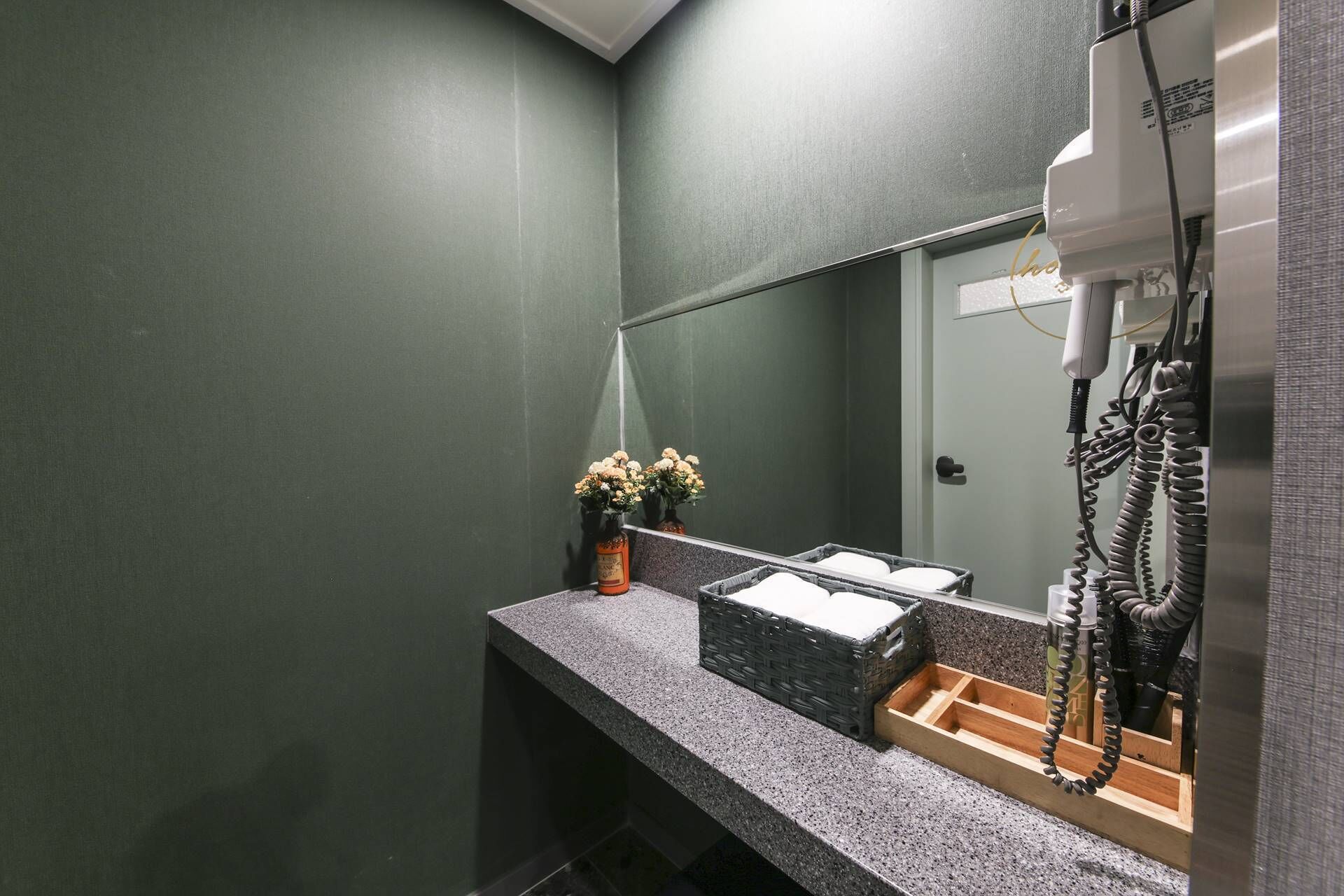 A modern bathroom with a granite countertop, a sink, a mirror, and a hairdryer on a stand.