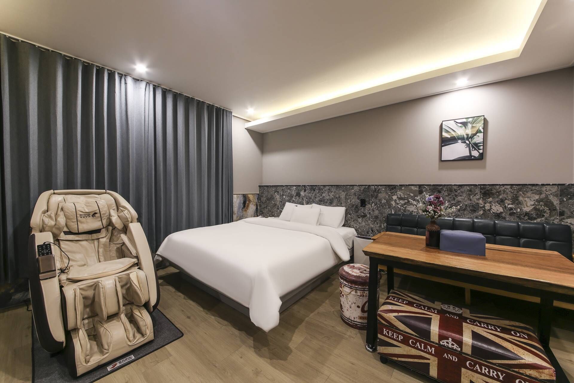 Habitación de hotel moderna con cama, sillón de masaje, mesa de comedor y vista a la ciudad.