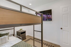 Ein Schlafzimmer mit Etagenbett, einem kleinen Nachttisch, einem an der Wand montierten Fernseher und einer Tür.