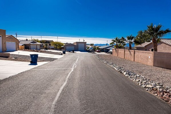 Une rue résidentielle bordée de maisons, un ciel dégagé et une poubelle bleue.