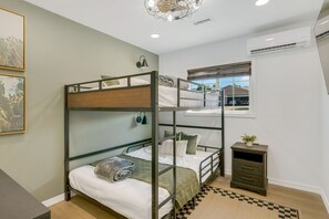 Une chambre avec un lit superposé, une fenêtre, un petit bureau et un tapis à carreaux.