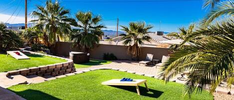 Un jardin avec une pelouse, des palmiers, un barbecue et un espace piscine.