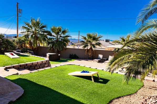 Un jardin avec une pelouse, des palmiers, un barbecue et un espace piscine.
