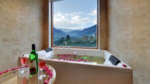 A bathroom with a bathtub filled with rose petals, a bottle of wine, and glasses on a table.