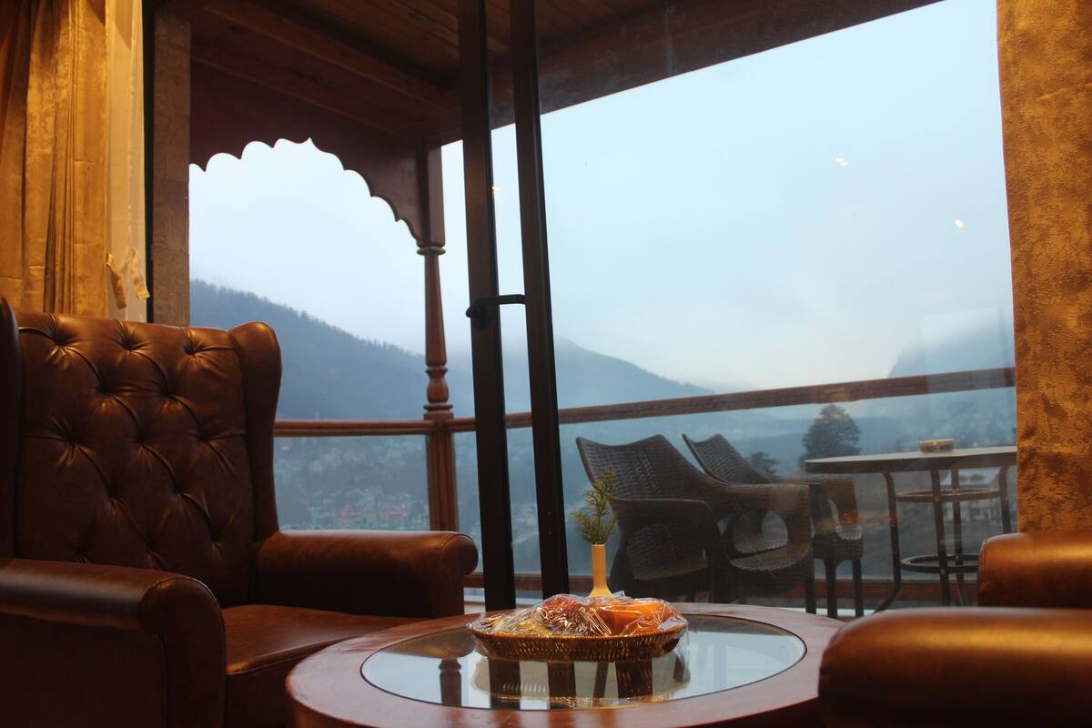 A cozy seating area with leather chairs and a glass table, overlooking a mountainous landscape through large windows.