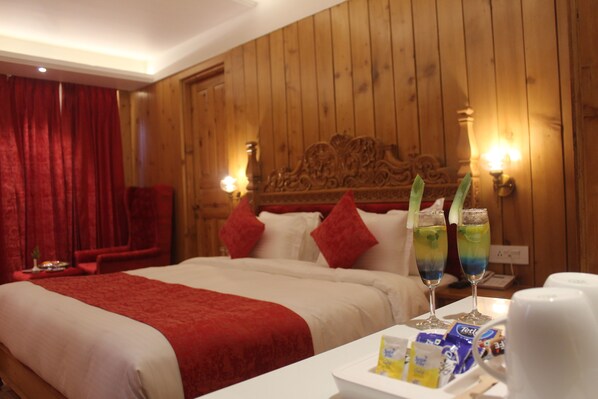 A hotel room with a wooden headboard, a red bedspread, and two bedside tables with lamps and a tray of snacks.