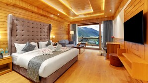 A hotel room with a large bed, a TV, a balcony with a mountain view, wooden walls, and a wooden ceiling.
