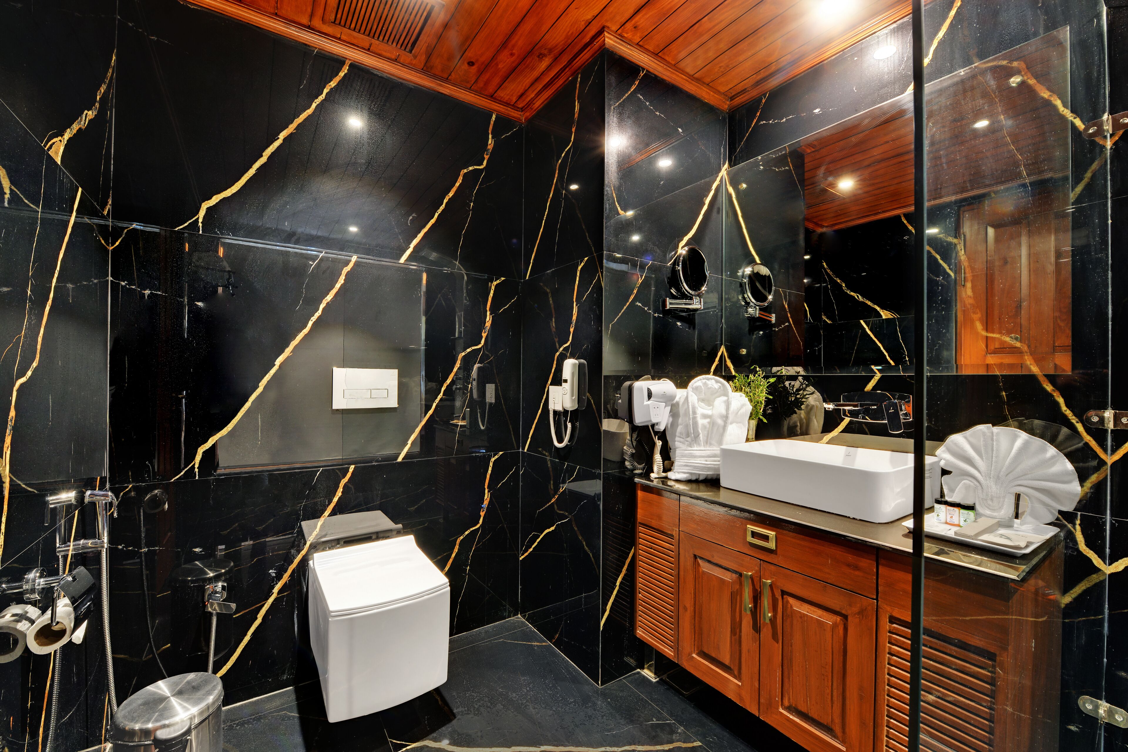 A modern bathroom with black marble walls, a wooden vanity, a white sink, and a glass-enclosed shower area.